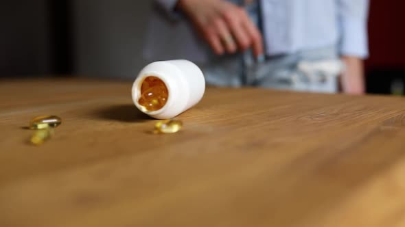 Woman's hand push bottle with yellow fish oil pills, and it falls out spills in to scatter contents