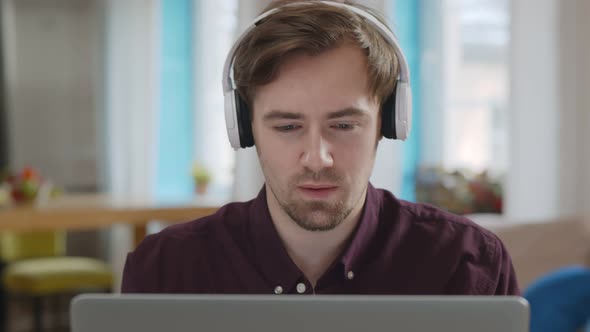 Handsome Smiling Young Man Using Laptop Computer Wearing Wireless Headphones