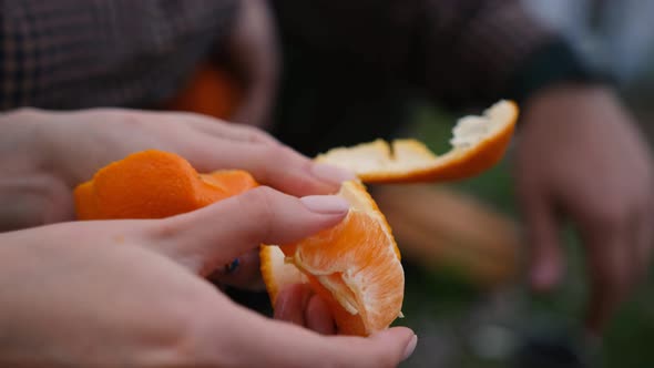 Slow motion 2x Woman hand peeling ripe sweet tangerine, close up above the fireplace in the forest