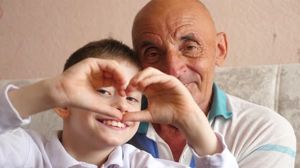 cheerful smiling caucasian boy 8 years old with grandfather 70-79 years old shows heart shaped hand 