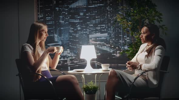 Two Young Business Women Speaking About Something at the Table with a Cup of Drink
