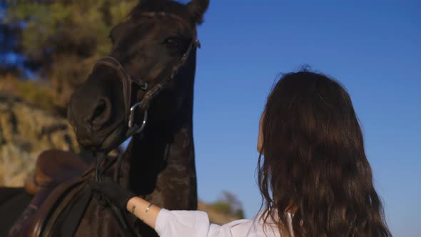 Closeup Young Slim Woman with Happiness Tattoo in Russian on Wrist Holding Bridle As Black Horse