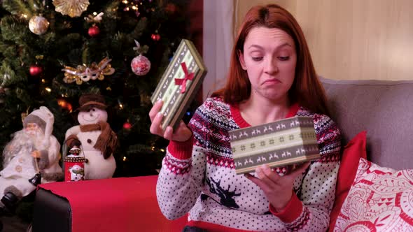 Sad Woman Lying on a Sofa Near the Christmas Tree, Opening Gift Disappointed and Unhappy
