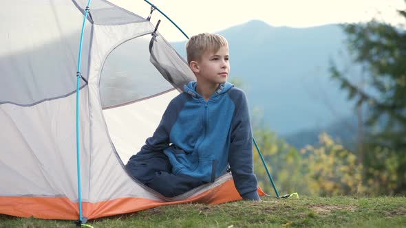 Hiker child boy sitting inside a tent in mountain campsite enjoying view of nature.