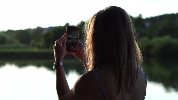 Backside shot of a girl taking photo of summer lake landscape; bokeh nature background