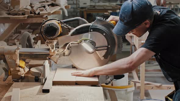 Man in a Carpentry Workshop Cutting a Small Pieces of the Wooden Detail Using a Big Circular Saw