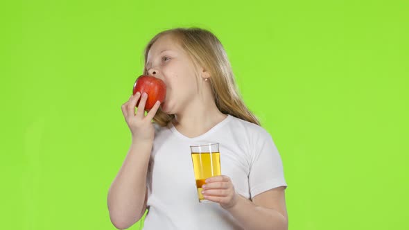 Little Girl Drinks Juice From a Glass and Holds an Apple. Green Screen