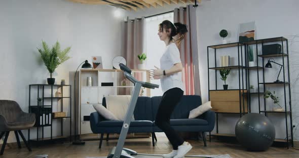 Woman Jogging on Treadmill at Home and Checking Indicators on Her smartwatch