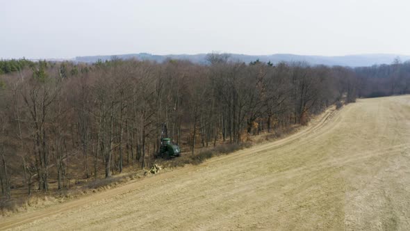 Forestry harvester vehicle on edge of dead leafless forest, drone shot.