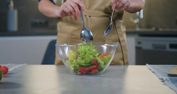 Hands Hold Spoons and Mixing Refreshing Vegetable Salad in Glass Bowl for Dinner 