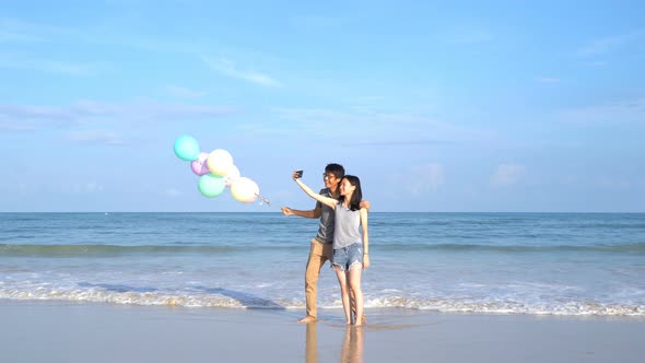 Happy Asian couple holding colorful balloons at the beach during travel trip on holidays