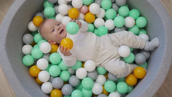 Happy Kid Lying in Soft Ball Pit Pool with Colorful Balls for Toddlers 9 Months Old Caucasian Baby