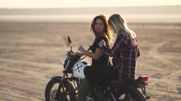 Attractive Young Woman Motorcyclist with His Girlfriend Riding a Motorcycle in a Desert on Sunset or