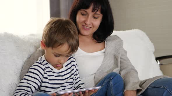 Mother and Son Spend Time Together Sitting on the Sofa and Watching a Movie with a Tablet