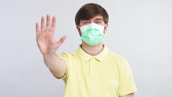 Sick Man in Sterile Mask Showing Stop Sign with His Arm To the Camera Wearing Yellow Shirt