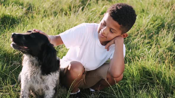 African Boy with Dog Sitting in the Grass on Sunset