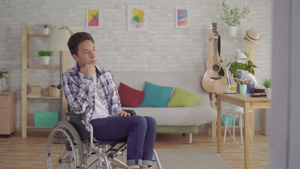 Sad Young Asian Man Disabled in a Wheelchair in the Living Room