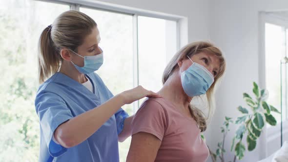 Female health worker stretching neck of senior woman at home