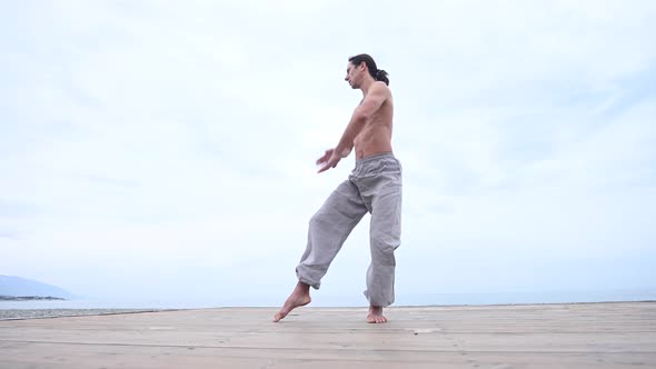 Caucasian Man with Naked Torso Practicing Wushu on the Seashore