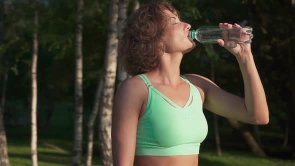 Beautiful sportive woman drinking water from a bottle after workout outdoors