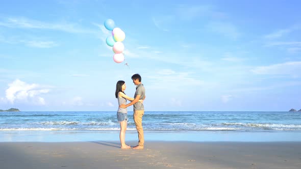 Happy Asian couple holding colorful balloons at the beach during travel trip on holidays