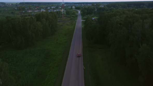 The red car is moving towards the village