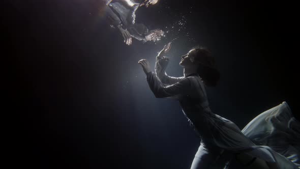 A Beautiful Woman in a Long Flowing Dress Floats Under the Water on a Dark Background She Swims To