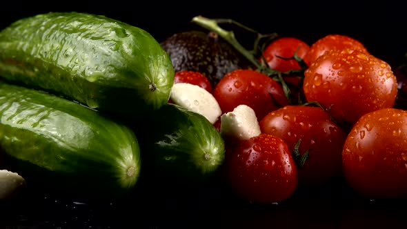 Cherry tomatoes, cucumbers, garlic, avocado and red onion on a black background in water drops