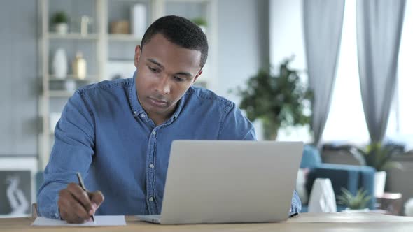 Young African Man Writing on Documents in Office