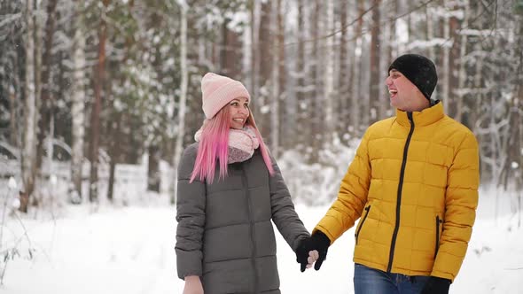 A Man in a Yellow Jacket and a Girl in a Hat and Scarf Walk Through the Winter Forest During a