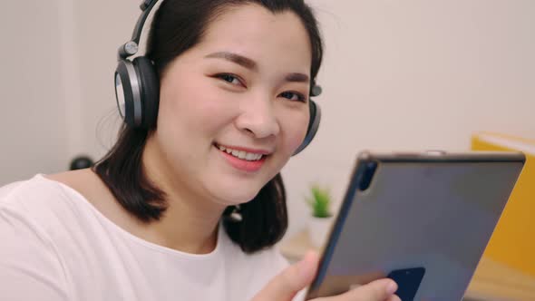 Beautiful asian woman look camera and smile relaxing and listening to music by tablet with headphone