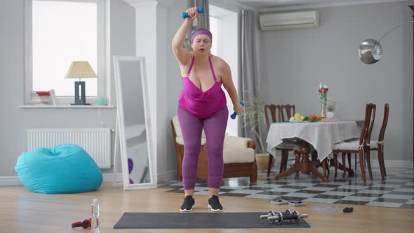 Persistent Serious Motivated Obese Woman Lifting Dumbbells Training at Home Indoors