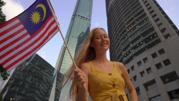 Slowmotion Shot of a Young Woman That Waves Malaysian Flag with Skyscrapers at a Background