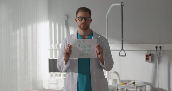 Portrait of Handsome Doctor Holding Safe Health Care System Sign in Hospital