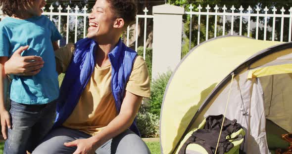 Happy biracial man and his son building tent together in garden