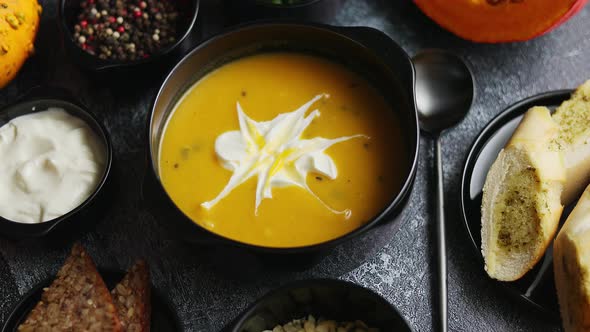 Delicious Pumpkin Soup with Cream Seeds Bread and Fresh Herbs in Elegant Ceramic Black Bowl