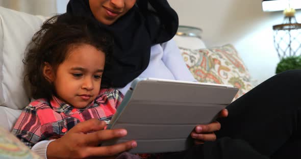 Young mother using a digital tablet with her daughter on the sofa at home 4k