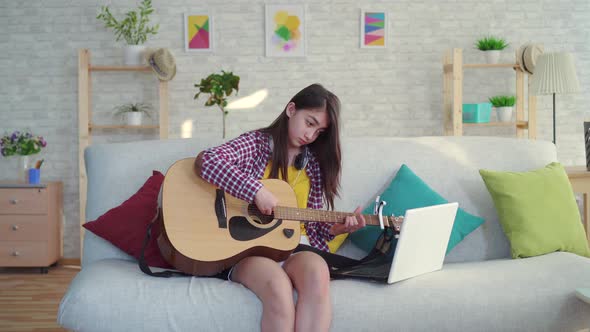 Beautiful Asian Girl with Long Hair in the Living Room of a Modern Home Studying Guitar Watching