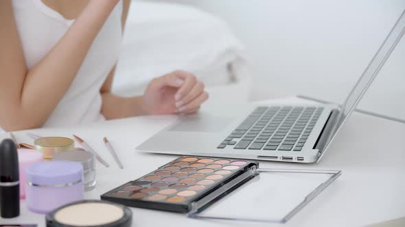 Hands of woman with learning makeup with brush on cheek on laptop computer with tutorial course.