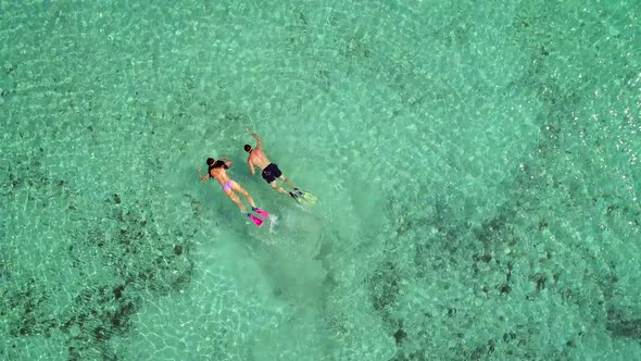 Aerial view of man and woman with masks and flippers diving in turquoise water.