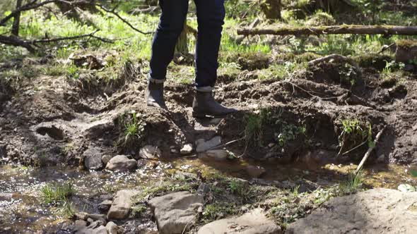 Young Man Crossing Brook in Forest