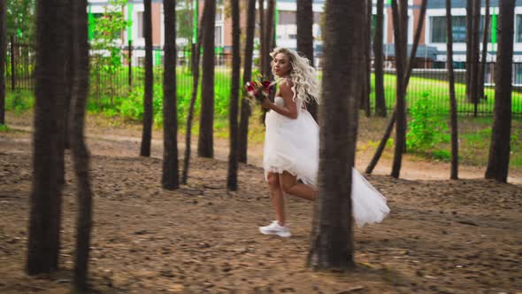 Blonde Bride in Wedding Dress and Sneakers Runs Along Forest