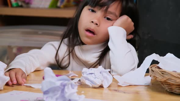 Upset little girl making a colorful drawing at home and crumpled the paper on desk.