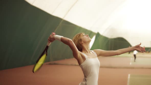 Young Woman with Muscular Body Wearing White Sportswear Hitting the Ball with Racket at Tennis Court