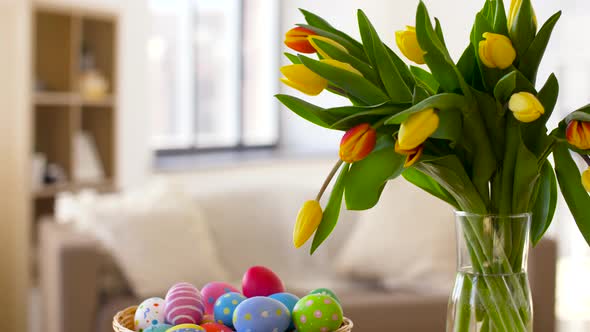 Colored Easter Eggs in Basket and Flowers at Home