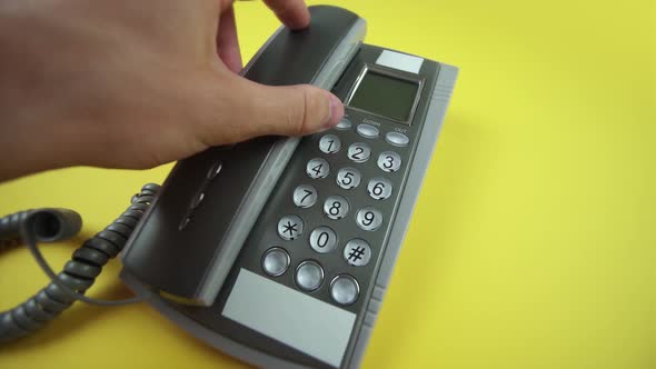 Person Puts Handset on Grey Corded Phone on Yellow Closeup