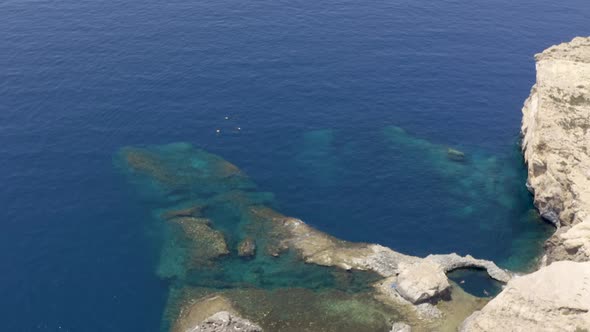 Group of scuba divers diving under a rocky cliff next to a rock,aerial.