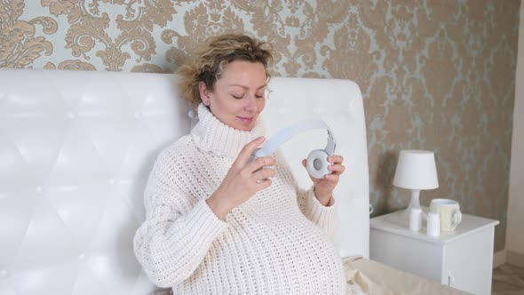 Young Pregnant Woman Listening Music And Putting Headphones on Her Belly During Pregnancy
