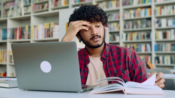 Sad Arabian or Indian Male Student Tired From Studying Sits at Desk in a Library Against the