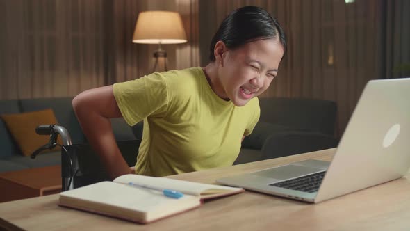 Asian Kid Girl Sitting In A Wheelchair Using Laptop Computer And Pain Her Back At Home alt